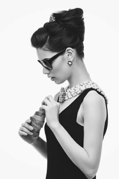 Beautiful young woman looking like audrey hepburn in sunglasses holding croissant