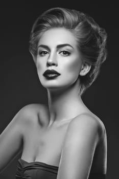 Beautiful young woman with dark lips and stylish hairdo. Beauty shot over dark grey background. Copy space.