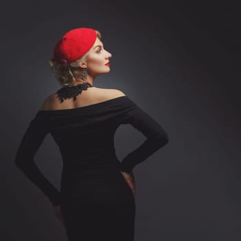 Back of beautiful lady in red beret standing over black background. Copy space. Studio shot.