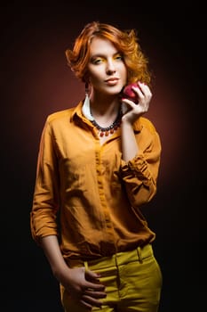 Beautiful young woman with bright yellow makeup dressed in orange autumn style holding red apple