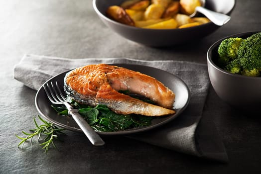 Grilled salmon steak with vegetables on dark background.