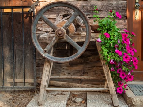 Weathered whetstone with handwheel and flowers at an old idyllic wooden hut in South Tyrol above the city of Merano.
