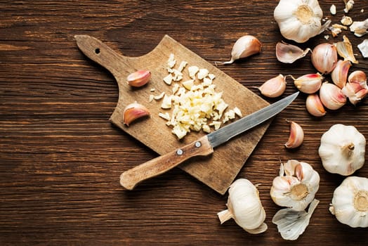 Slicing garlic with a knife on a wooden vintage table.