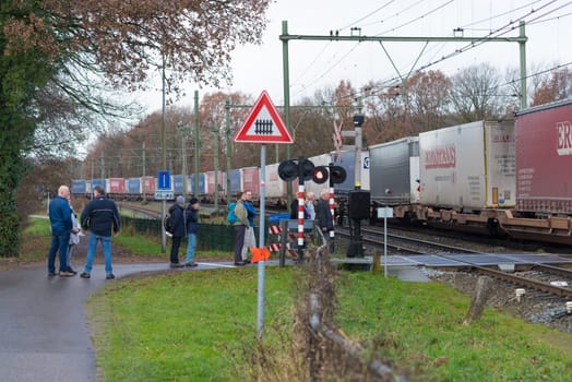 OLDENZAAL, NETHERLANDS - NOVEMBER 27, 2016: Unknown people waiting for a passing container train on a secured train crossing