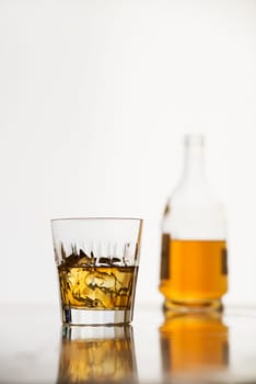 Whiskey with ice in glass and bottle on white background