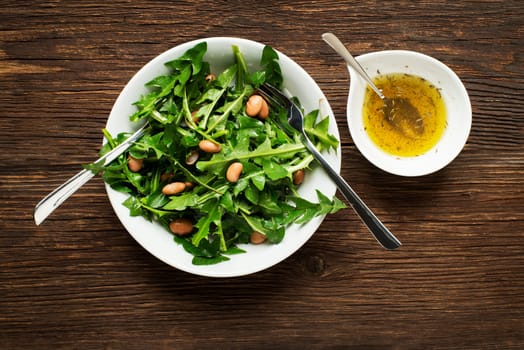 Fresh dandelion salad with beans on wooden background
