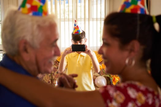 Family celebrating senior man birthday in retirement home. Patient dancing with daughter in hospital and child taking photo.