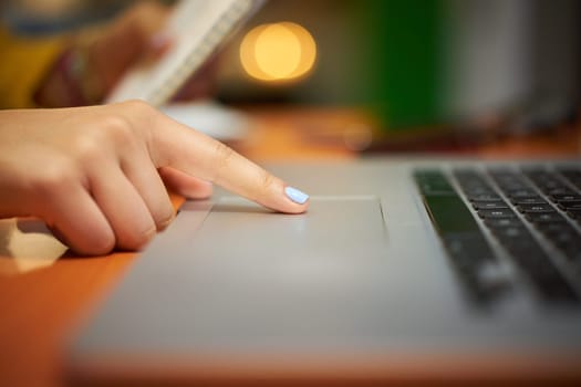Young woman clicking on trackpad of laptop computer. Female student studying at night and using pc at home. Copy space.