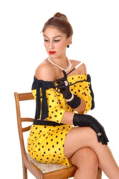 A beautiful young woman in a yellow dress holding a long cigarette .holder sitting on a chair, looking away, isolated for white background..