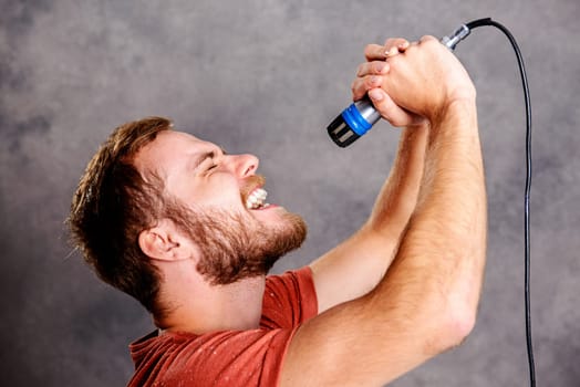 young bearded man in red shirt singing in microphone