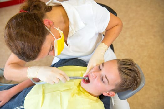 teenager is treated by female dentist in dental surgery