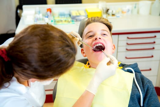 teenager is treated by female dentist in dental surgery