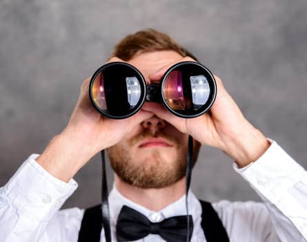 young bearded man in white shirt and bow tie looking through a binoculars