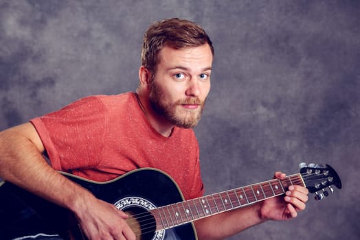 young bearded man in red shirt playing acoustic guitar