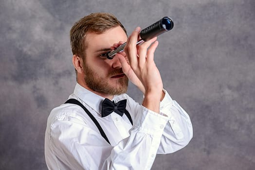 young bearded man in white shirt and bow tie looking through a telescope