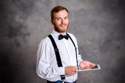 young bearded man in white shirt and bow tie using tablet PC