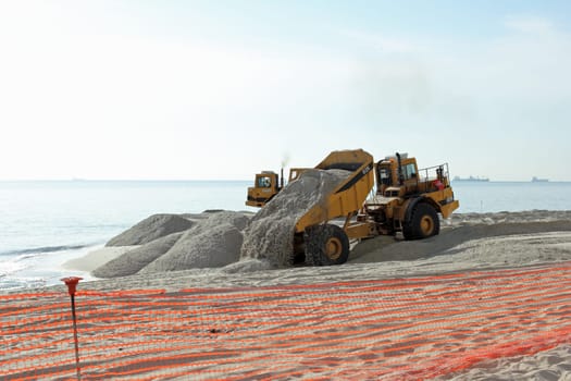 Fort Lauderdale, FL, USA - March 3, 2016: Piles of sand dumped on the beach shore replenish and widen. Large trucks restore sand on the coast expanding the beach.