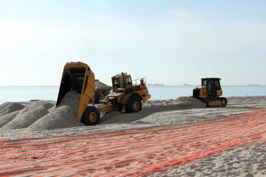 Fort Lauderdale, FL, USA - March 3, 2016: Two dump trucks and a bulldozer work on beach nourishment on the coast. Earth moving equipment add sand to a public beach.