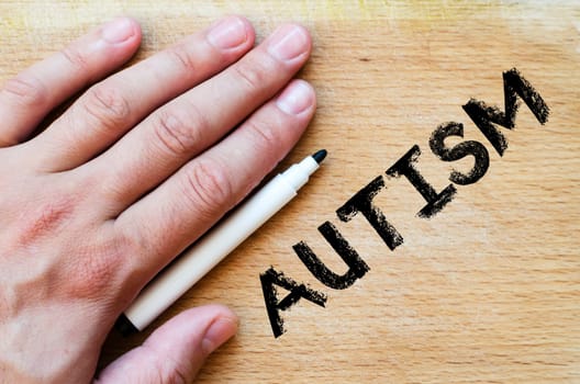 Human hand over wooden background and autism text concept