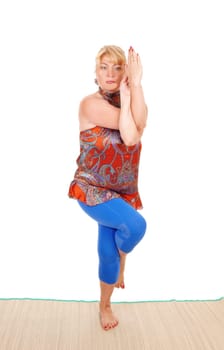 A beautiful blond woman standing on the floor showing some nice yoga.poses, in a blue pants, isolated for white background..