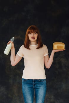Woman standing against a studio background with a glass of milk and a loaf of bread in each hand.