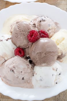 Scoops of chocolate ice cream in the white plate with raspberries