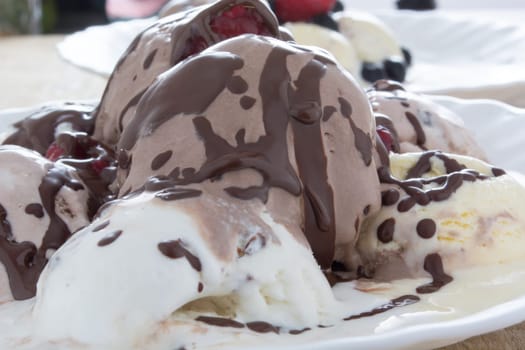 Scoops of chocolate ice cream in the white plate with raspberries and chokeberries
