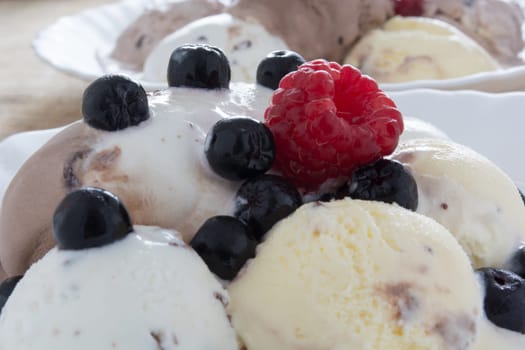 Scoops of chocolate ice cream in the white plate with raspberries and chokeberries