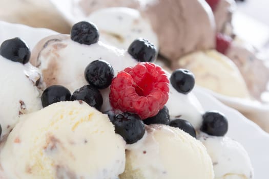 Scoops of chocolate ice cream in the white plate with raspberries and chokeberries