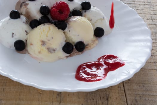 Scoops of chocolate ice cream in the white plate with raspberries and chokeberries