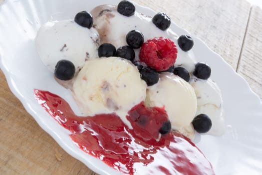 Scoops of chocolate ice cream in the white plate with raspberries and chokeberries