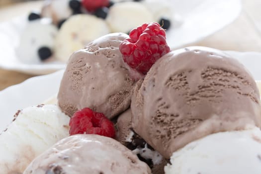 Scoops of chocolate ice cream in the white plate with raspberries