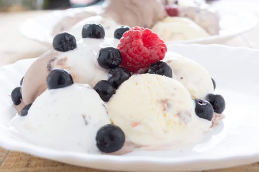 Scoops of chocolate ice cream in the white plate with raspberries and chokeberries