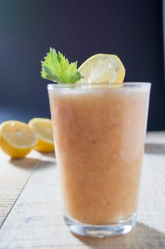 Fresh lemonade with ginger decorated with green celery leaves and lemon on the dark background