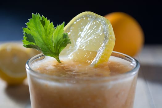 Fresh lemonade with ginger decorated with green celery leaves and lemon on the dark background