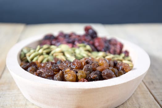 Bowl full with dry fruits and pumpkin seeds on the wooden table, shoot with selective focus