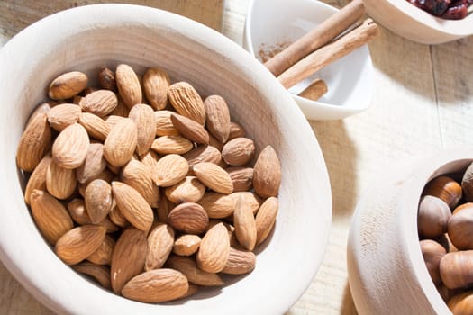 Bowl full with almonds on the wooden table with various spices and ingredients on the table around it