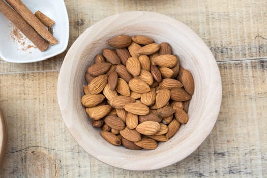 Bowl full with almonds on the wooden table with various spices and ingredients on the table around it