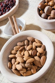 Bowl full with almonds on the wooden table with various spices and ingredients on the table around it