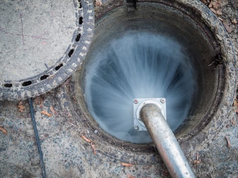 Open sewer access with escaping water jet on the suspended high-pressure water pipe