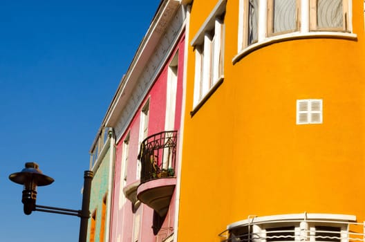 A curve of orange joins with a small balcony on a pink wall, and completes the journey with a street lamp in Valparaiso, Chile
