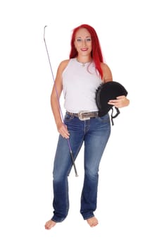 A happy woman with her rider helmet and whip, with long red hair.standing isolated for white background..