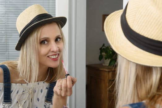 beautiful smiling blond woman with mirror putting lip-gloss
