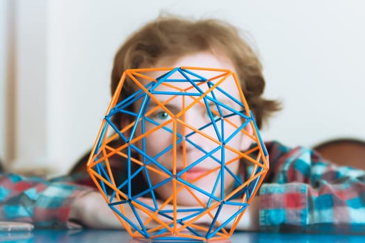 Coloured three-dimensional model of geometric solid against the background of the young man's face defocused. Selective focus on foreground.