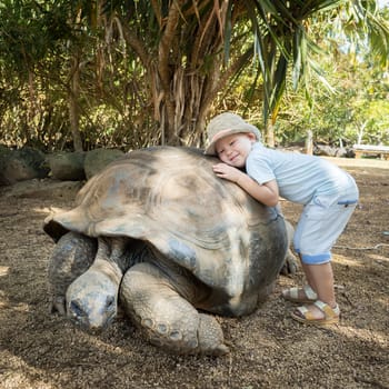 Child huggging Aldabra giant tortoise. Mauritius