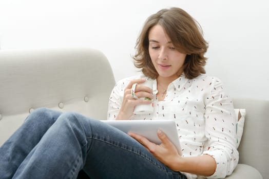 beautiful young woman with a tablet drinks a cup of tea