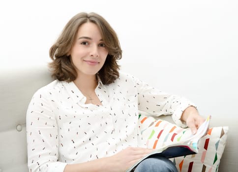 beautiful young woman reads a book sitting on the sofa