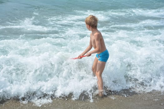Little blond boy with blue swimming trunks stands with a net directly in the sea - wave
