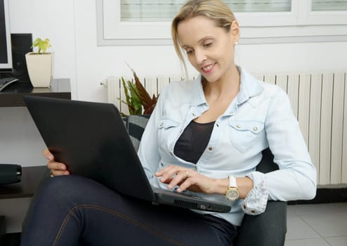 pretty young blonde woman uses a laptop in the sofa