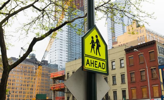 yellow traffic sign in New York of school zone with crossing children with the word ahead